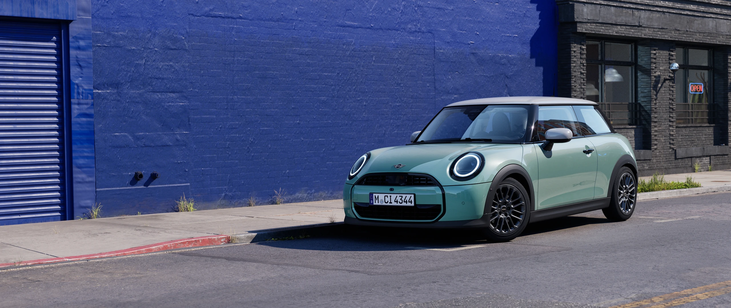 MINI Cooper в цвете Ocean Wave Green, припаркованный на городской улице рядом с синей стеной.