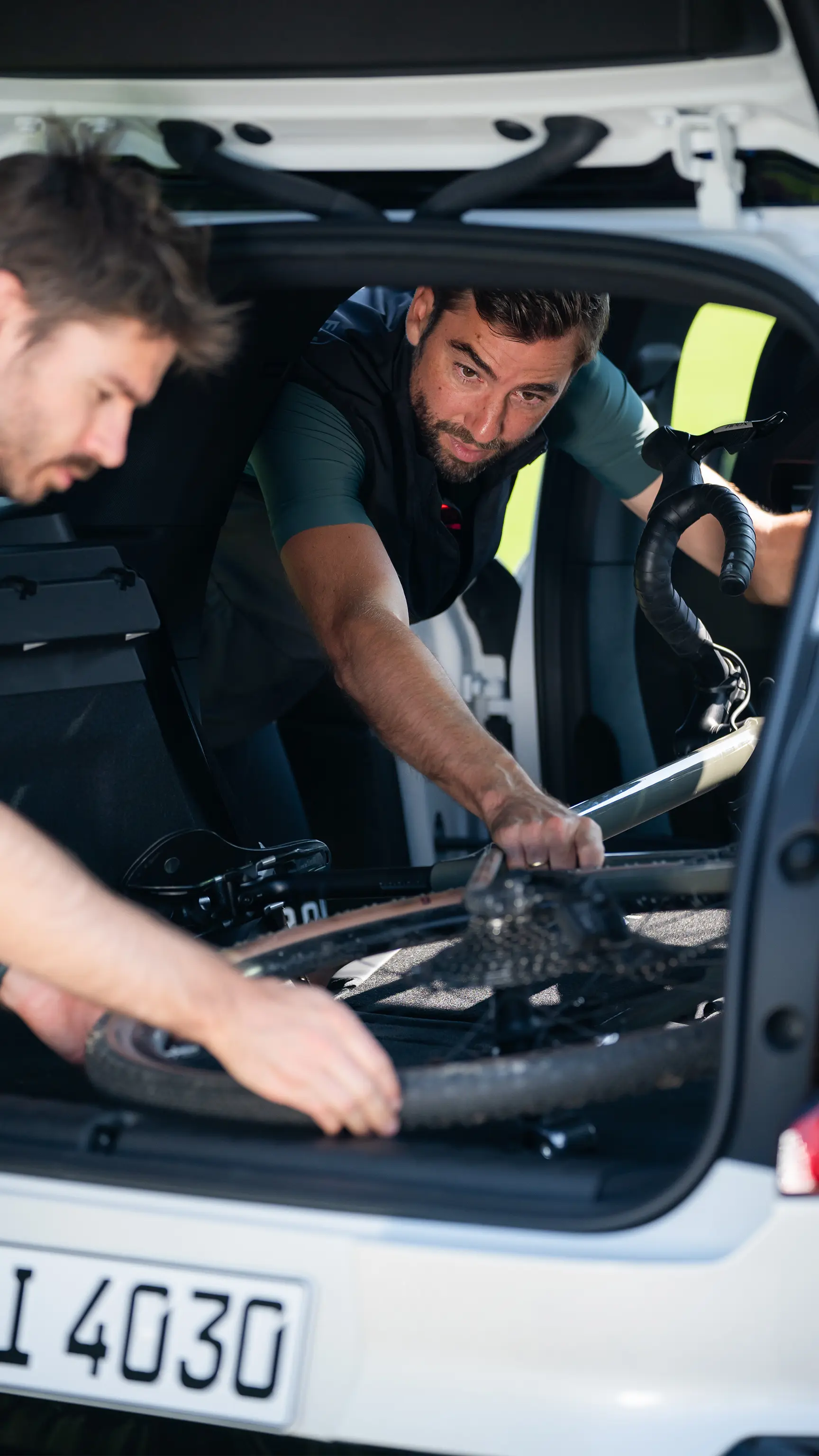 Два человека загружают велосипед в заднюю часть автомобиля MINI через открытый багажник.