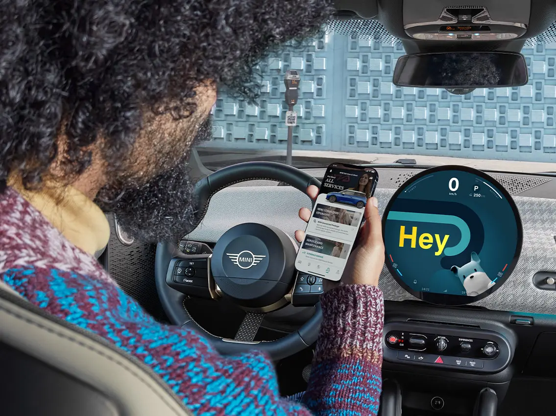 Мужчина сидит в автомобиле MINI и смотрит в свой мобильный телефон